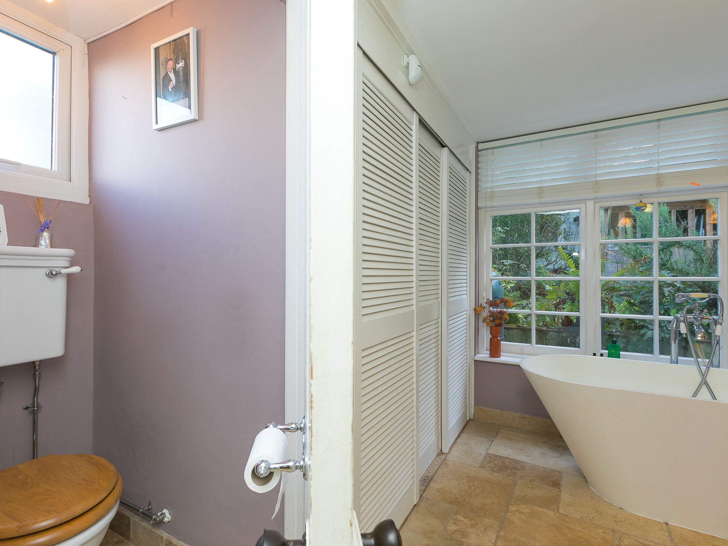 Un baño con inodoro, lavabo, ventana con persianas y bañera.