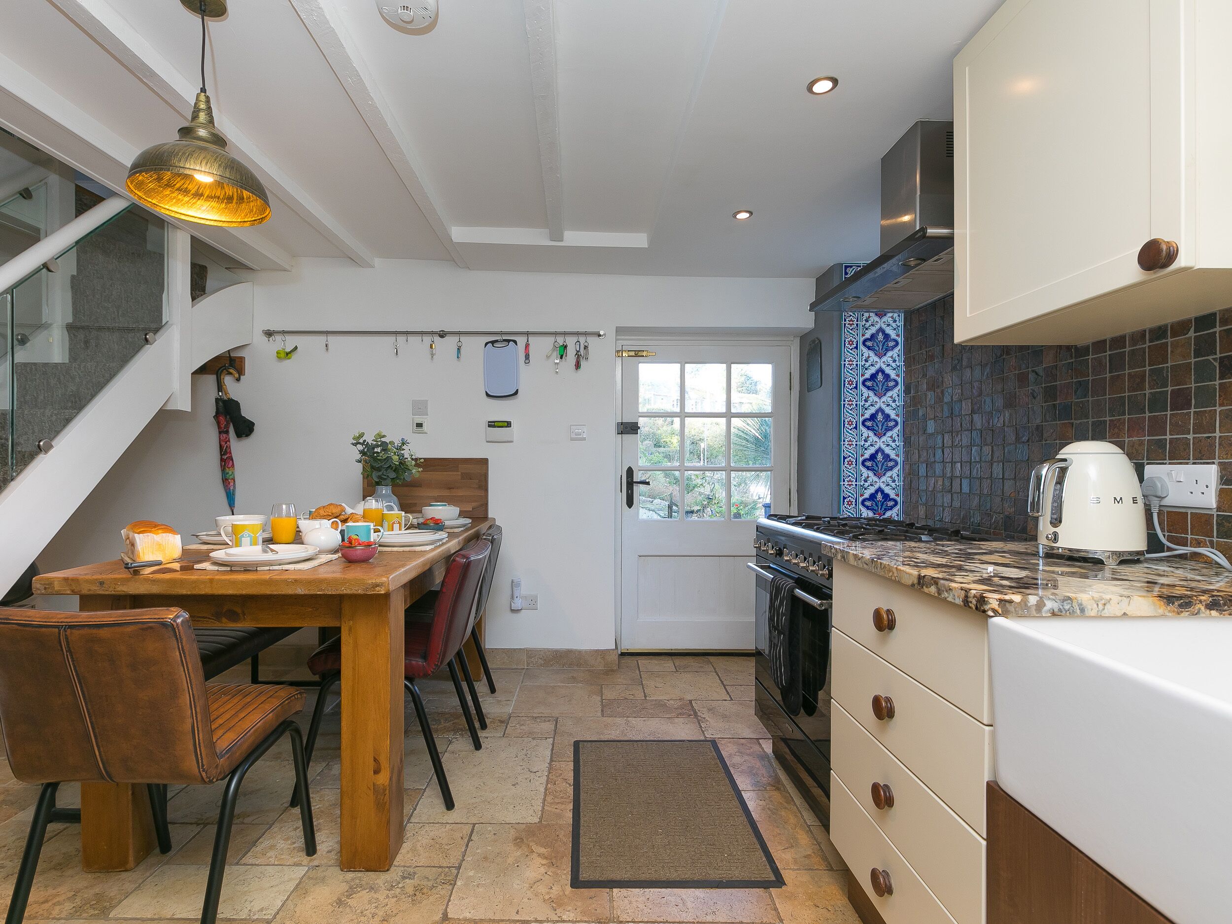 A modern kitchen with a dining area, featuring a wooden table, chairs, and a hanging light fixture.
