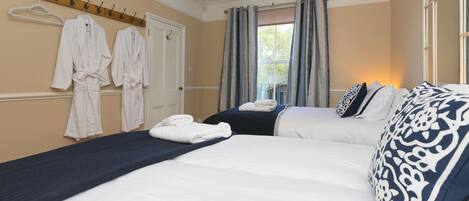 A hotel room with two beds, a hanging robe rack, and a window with curtains.