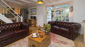 A spacious living room with two leather sofas, a wooden coffee table with a plate of food and drinks, and a large window offering a view of the outdoors.