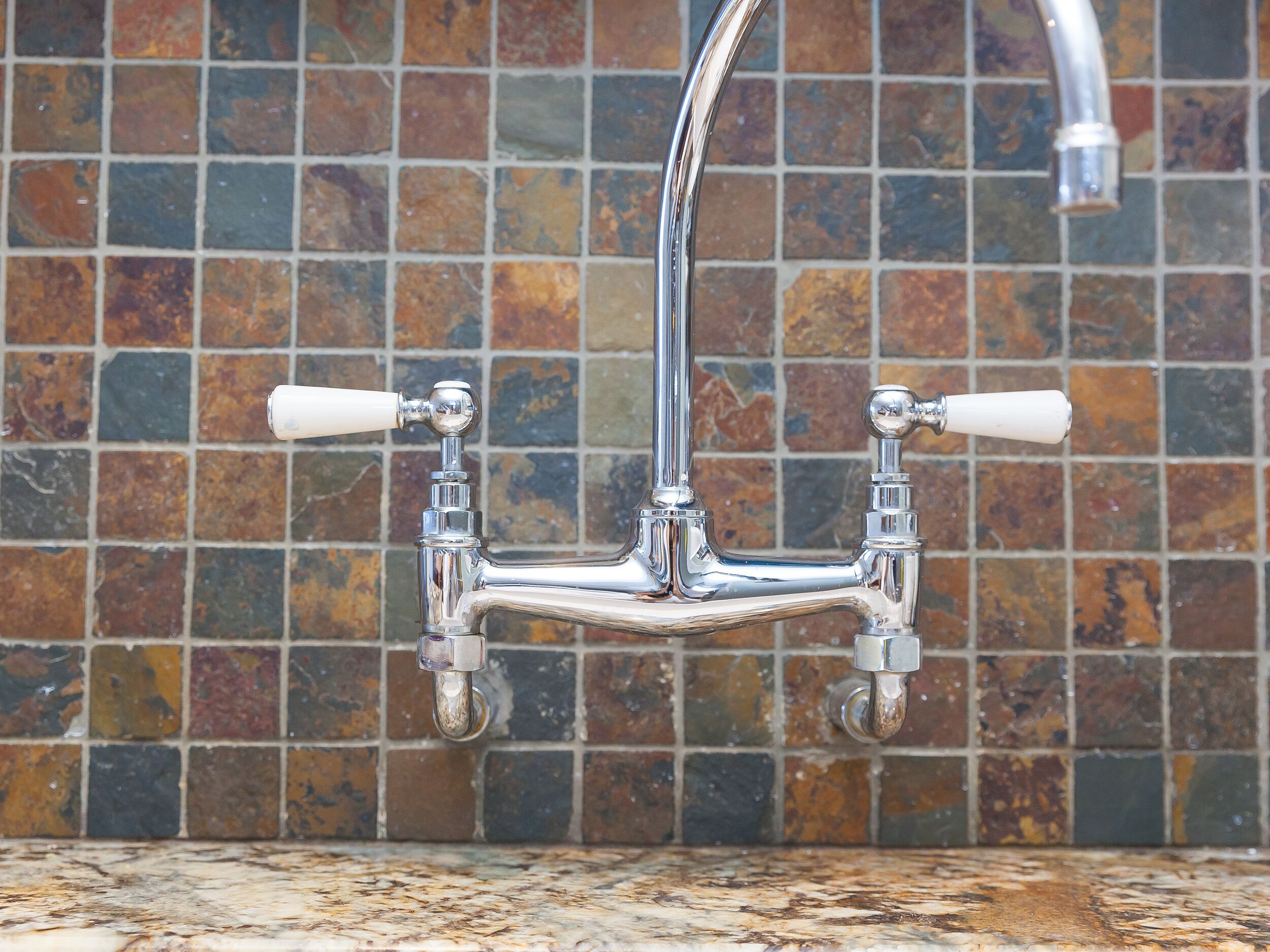 A chrome faucet with two handles against a tiled backsplash.