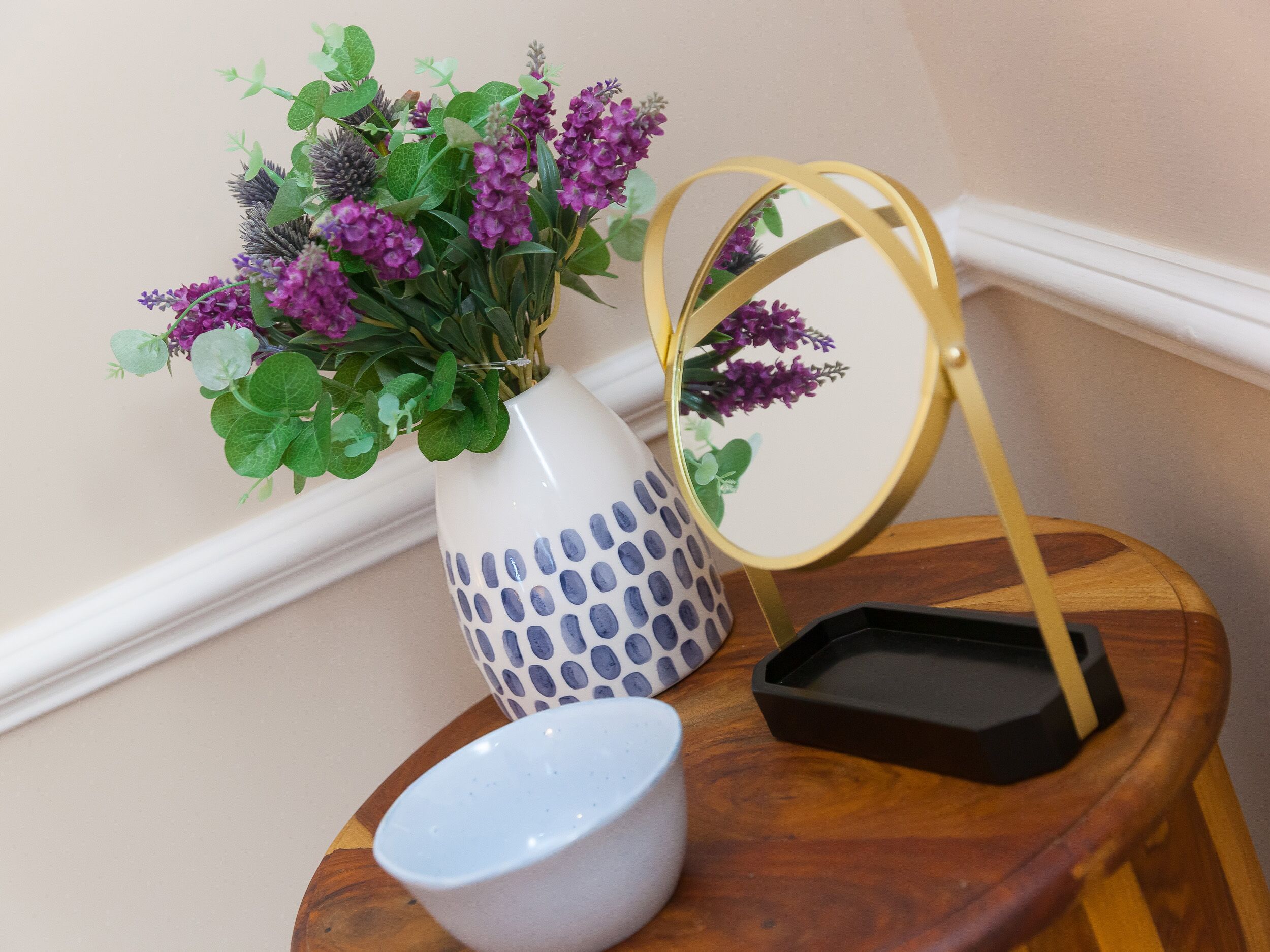 Un vase blanc orné de motifs bleus, un miroir et un bol posés sur une table en bois.