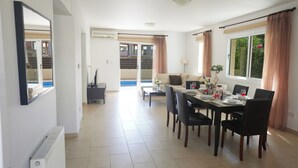 A dining area with a table set for four, a sofa, and a view of a balcony. - Protaras Holiday Villa Cl19 (Paralimni)