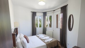 A bedroom with a bed, a bedside table, a window with curtains, and a mirror on the wall. - Protaras Holiday Villa Cl19 (Paralimni)