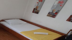 A single bed with a wooden frame, white bedding, and a yellow blanket. There are two wall decorations with floral designs. - Apartment Marijana (Obrovac)
