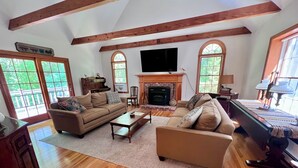 A spacious living room with wooden floors, a fireplace, and large windows. - Sprawling Home With Private Association Lake Access (2289) (Orleans)