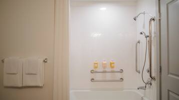 A bathroom with a bathtub, a shower with a handheld showerhead, and a towel rack with two towels. There are also three bottles of shampoo or conditioner on a shelf.