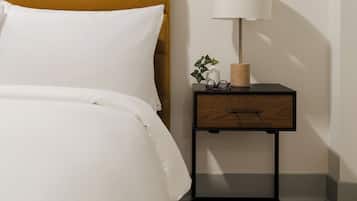 A neatly made bed with white linens, a mustard-colored headboard, a bedside table with a lamp, and a framed picture on the wall.