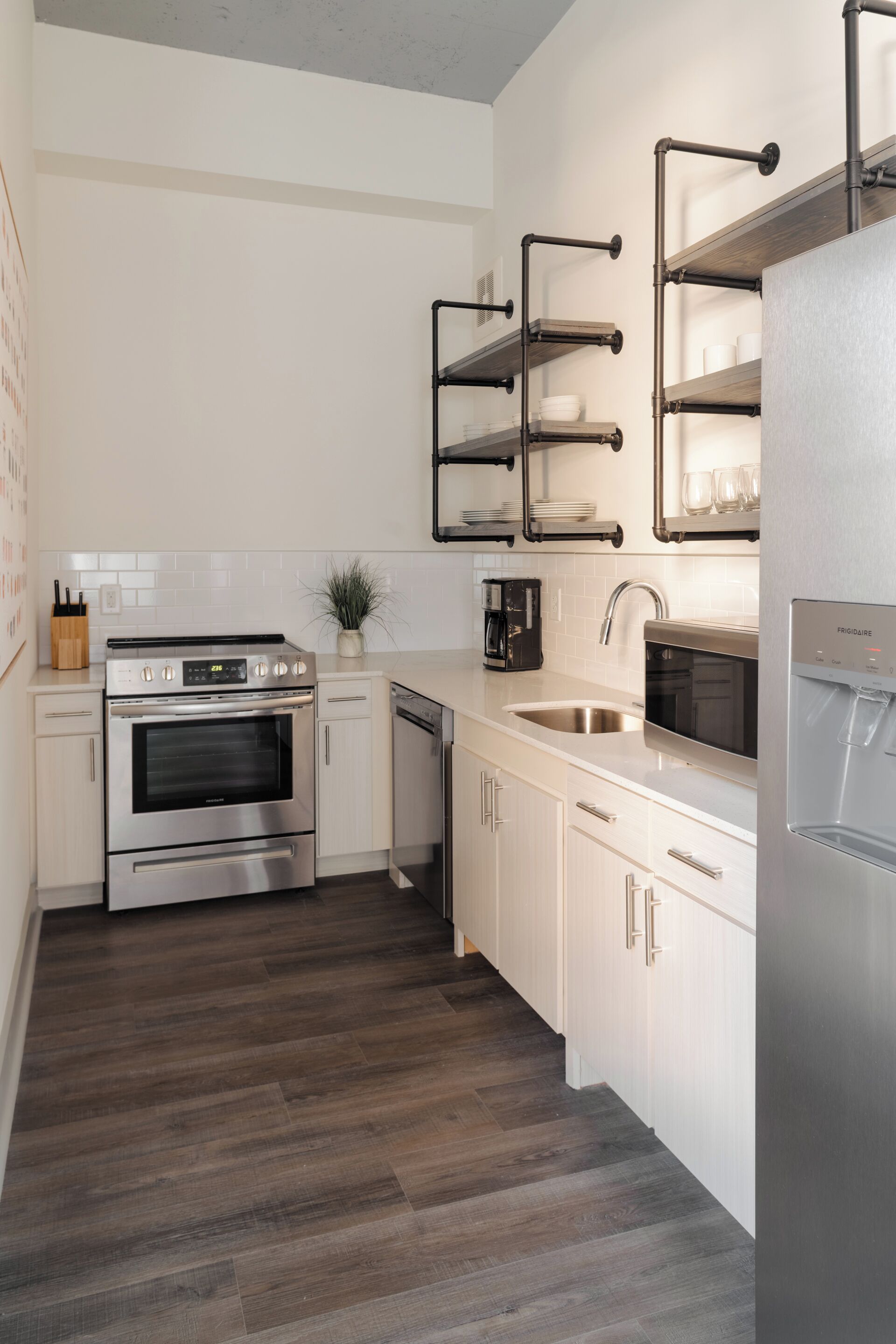 Une cuisine moderne dotée d’appareils électroménagers en acier inoxydable, de meubles blancs et d’un plancher en bois.