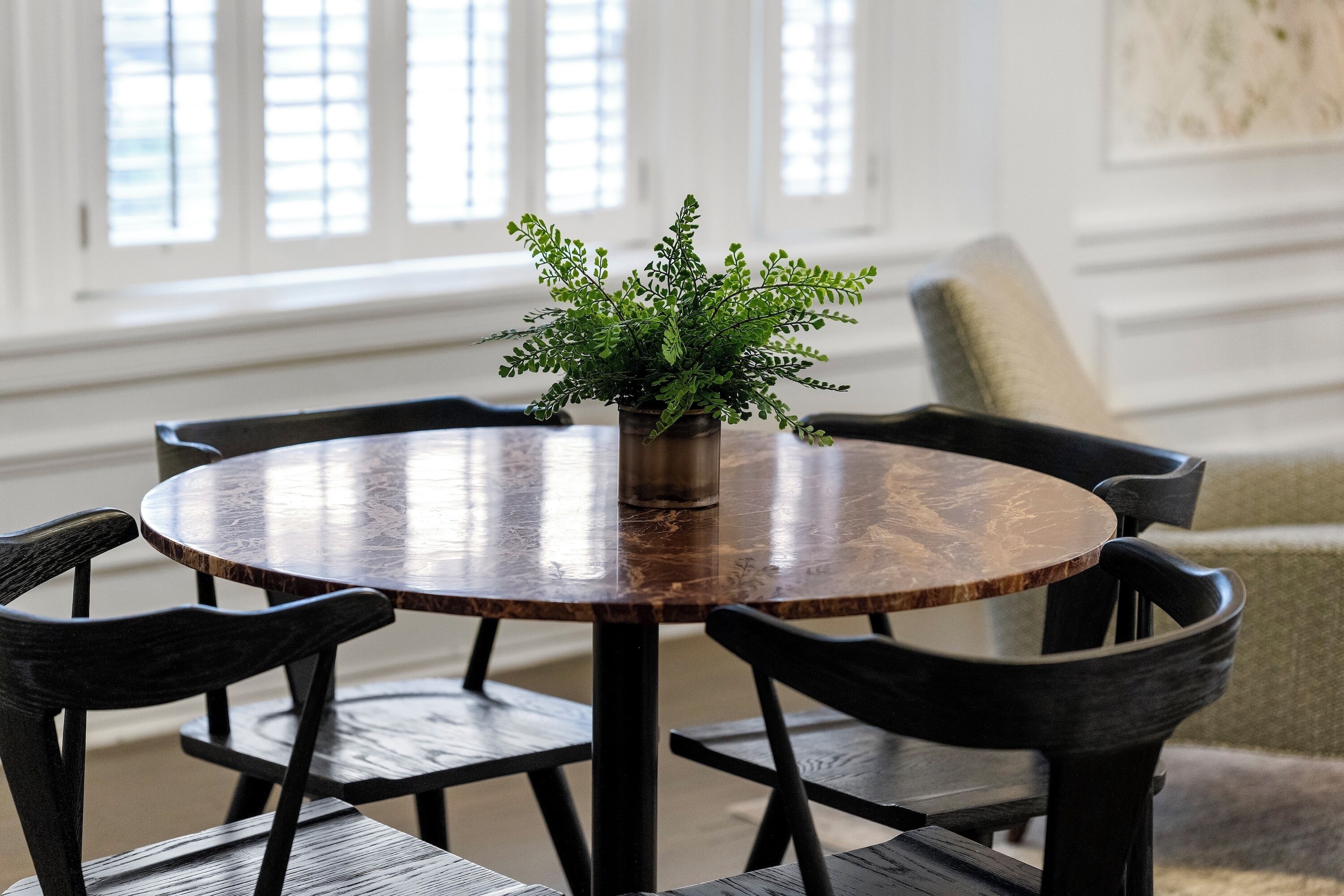 A round wooden table with a potted plant in the center, surrounded by four dark wooden chairs.