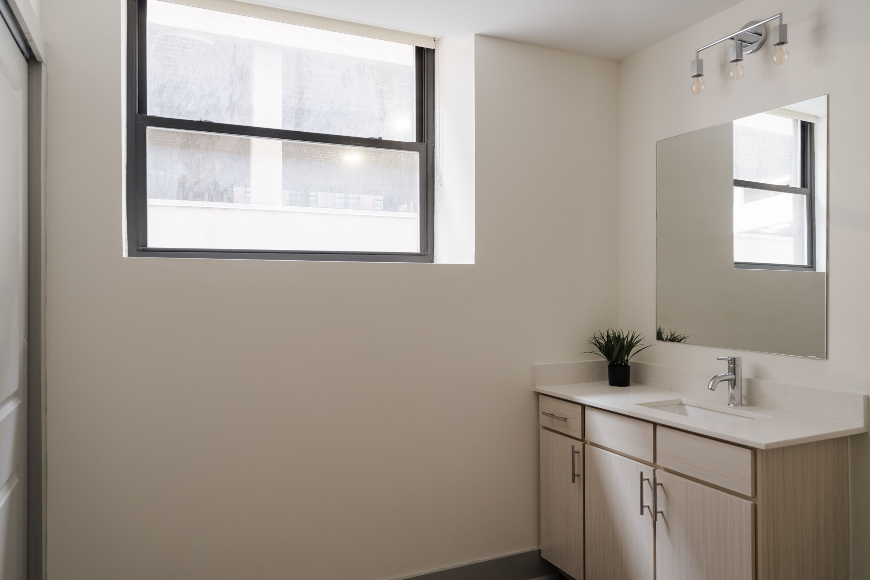Ein Badezimmer mit Fenster, Waschbecken, Spiegel und Schränken.