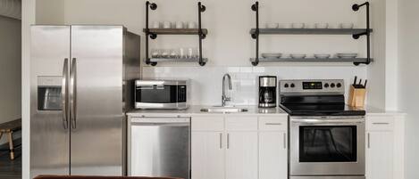 A modern kitchen with stainless steel appliances, white cabinetry, and a brown chair.