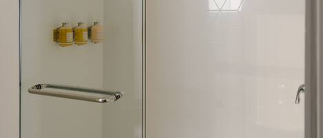 A glass-enclosed shower with a glass door, a handrail, and a showerhead.