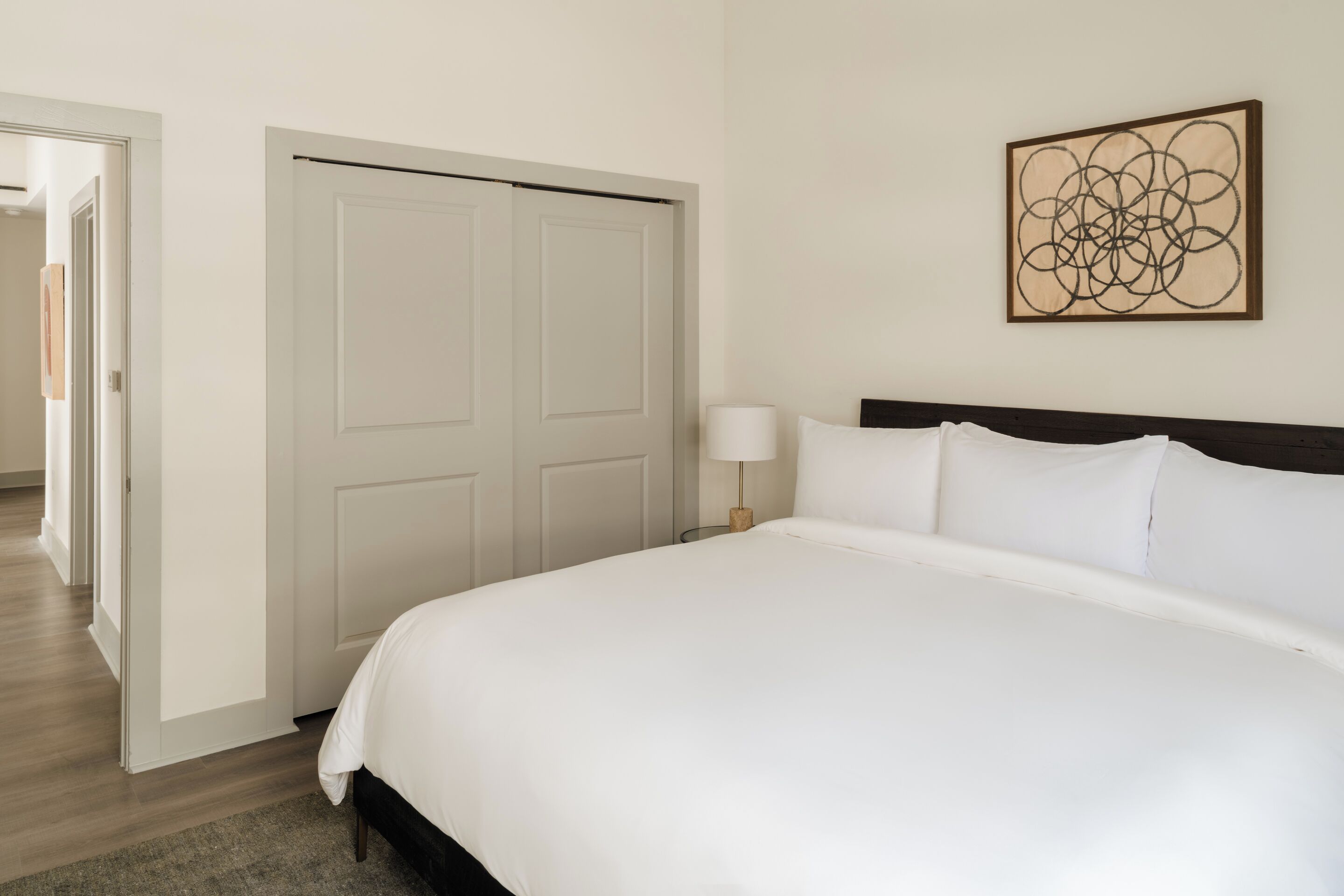 A neatly arranged bedroom with a large bed, a closed door, and a wall-mounted abstract art piece.
