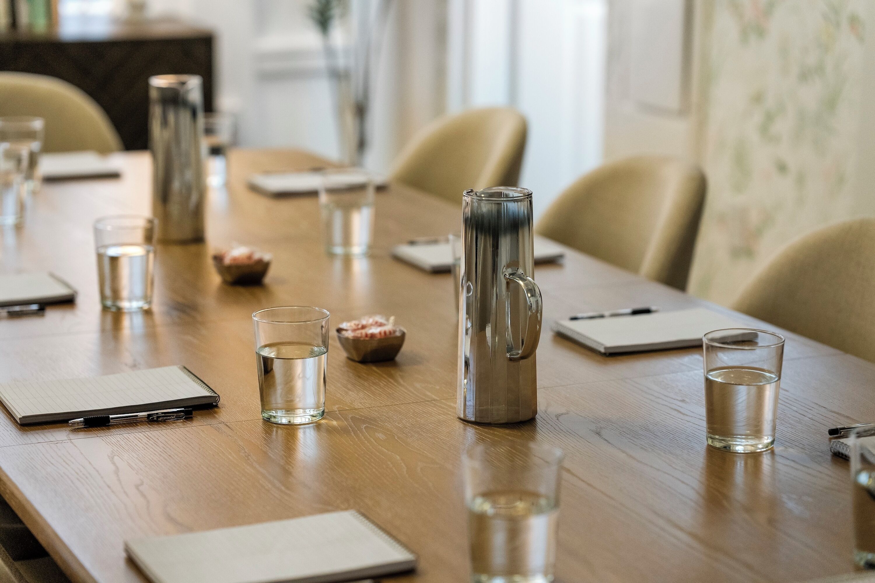 A conference table with water glasses, a thermos, notepads, and pens.