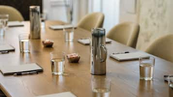 A conference table with water glasses, a thermos, notepads, and pens.