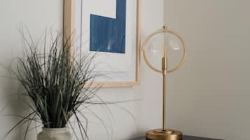 Une table de chevet noire ornée d’un tableau encadré, d’une plante en pot, d’une lampe et d’un magazine.