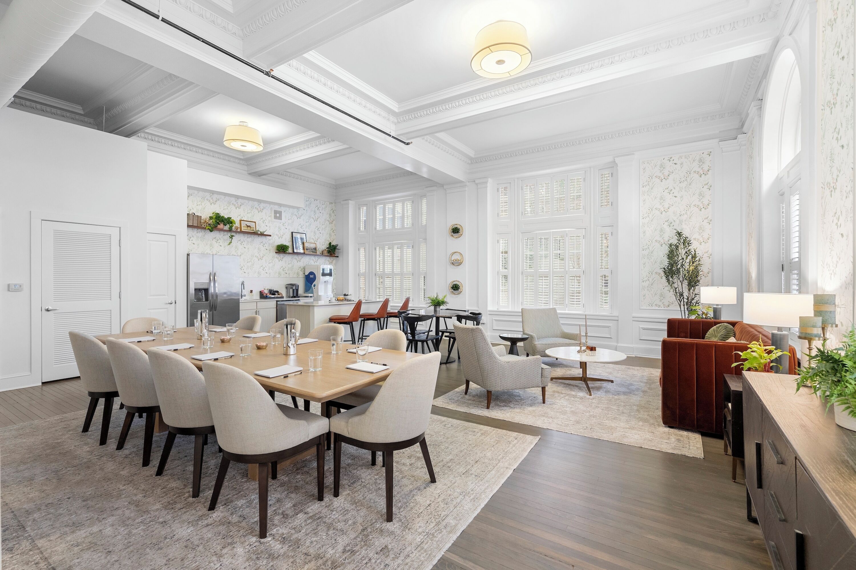 A spacious dining area with a long wooden table and multiple chairs, a cozy seating area with a red sofa and armchairs, and a kitchen area with modern appliances.