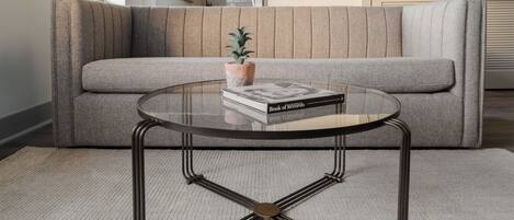 A modern living room with a grey sofa, a glass coffee table with a metal frame, and a small potted plant.