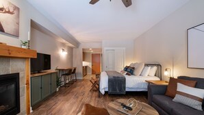 A modern, well-lit room with a bed, a sofa, a coffee table, a TV, and a fireplace. - Premium Unit 3318 - Studio - Fraser Crossing/founders Pointe Condo (Winter Park)