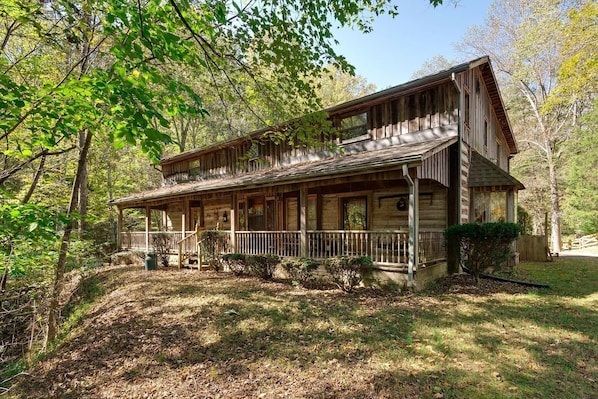 A rustic wooden cabin with a porch, surrounded by trees and a grassy area.