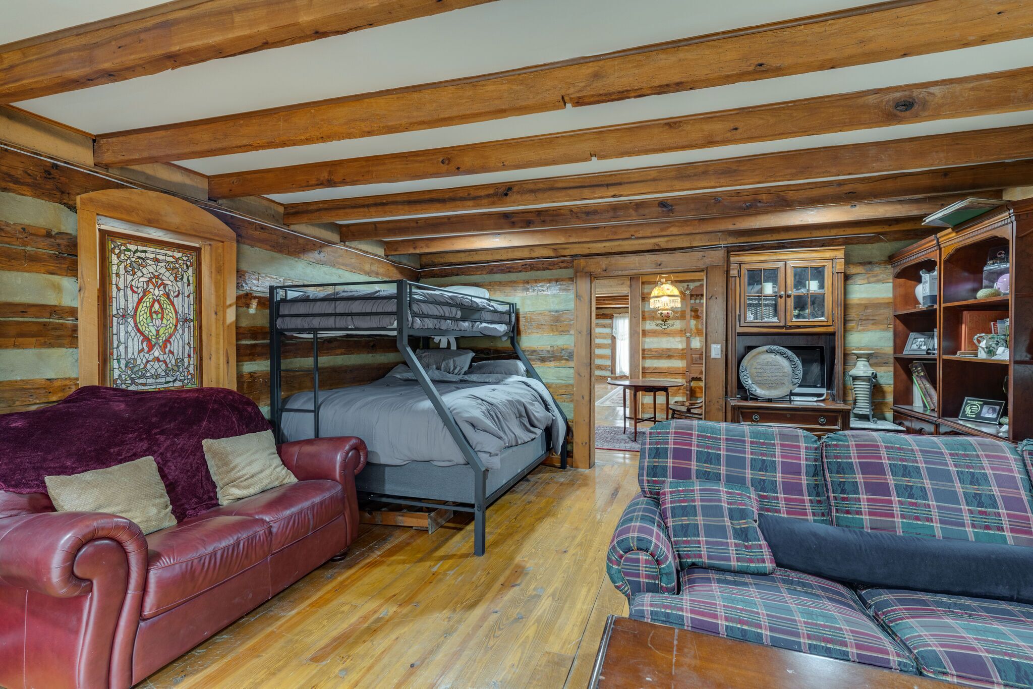 A log cabin interior with a bunk bed, a red leather sofa, and a plaid sofa.