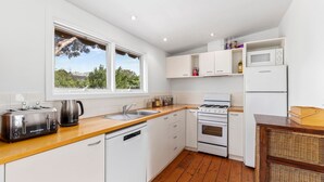 Cocina moderna con armarios blancos, encimera de madera, estufa a gas, lavavajillas, microondas y refrigerador.