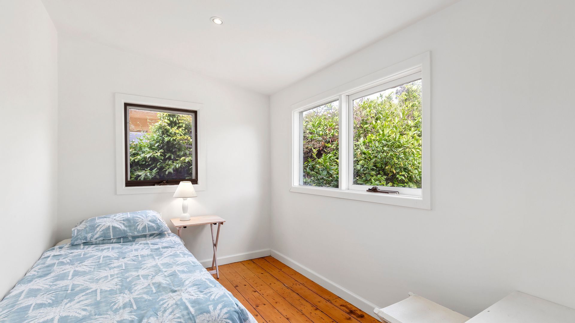 A bedroom with a bed, a nightstand, a lamp, and a window with a view of greenery.