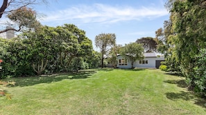 A residential property with a well-maintained lawn, a detached house with a garage, and mature trees surrounding the yard. - Springs Beach House - Point Lonsdale (Point Lonsdale)