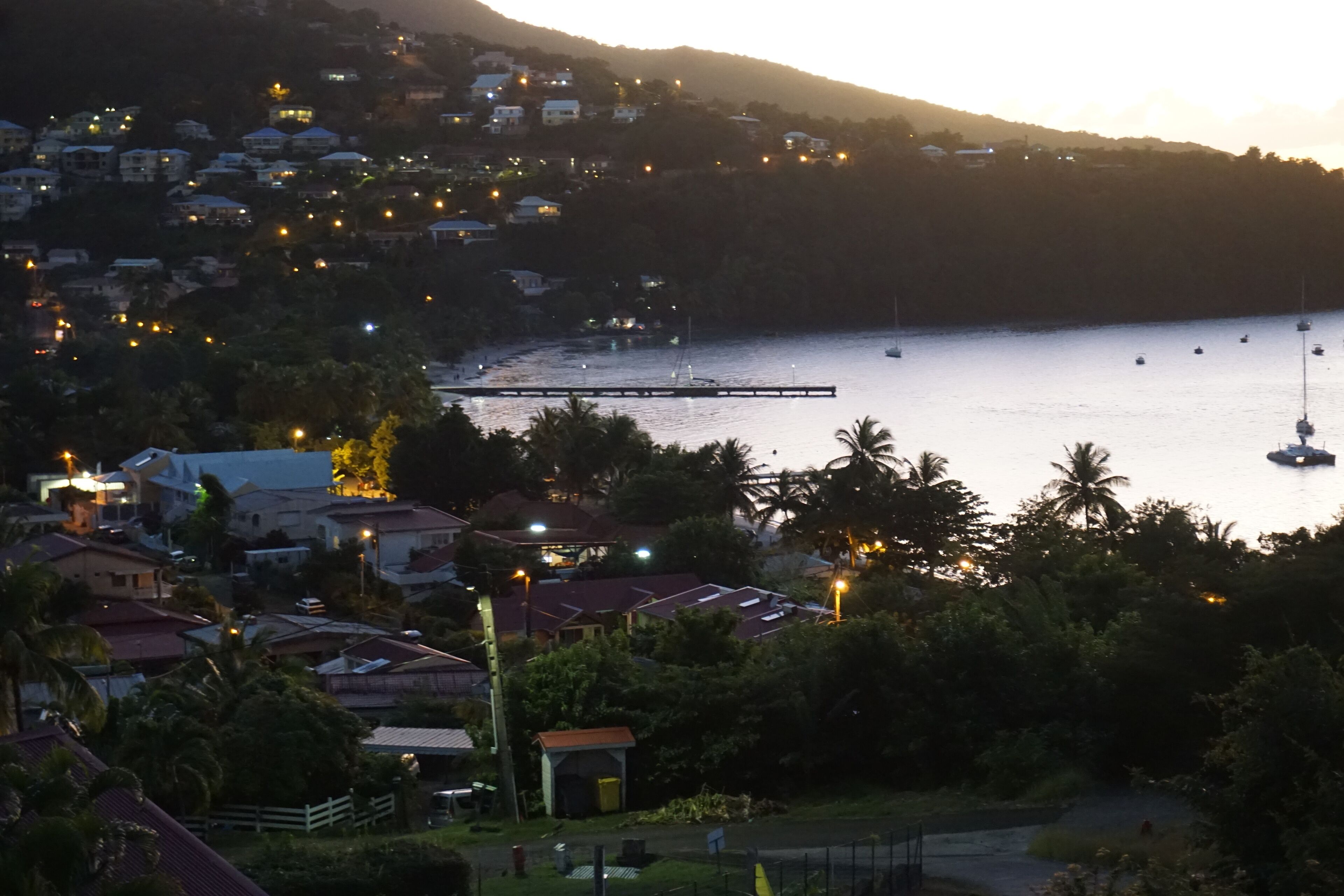 Une ville côtière au crépuscule, avec des maisons, un quai et des bateaux.