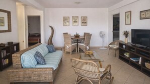 A living room with a sofa, chairs, a dining table, a TV, and framed pictures on the wall. - 3-bedroom apartment with panoramic view of Anse à l'Ane bay, 2 steps from the beach (Les Trois-Îlets)