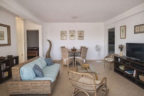 Un salon avec un canapé, des fauteuils, une table à manger, un téléviseur et des tableaux encadrés accrochés au mur.