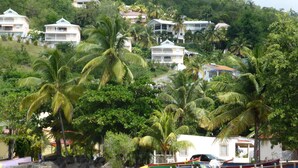 A beachfront property with a sandy beach, palm trees, and a row of boats. - 3-bedroom apartment with panoramic view of Anse à l'Ane bay, 2 steps from the beach (Les Trois-Îlets)