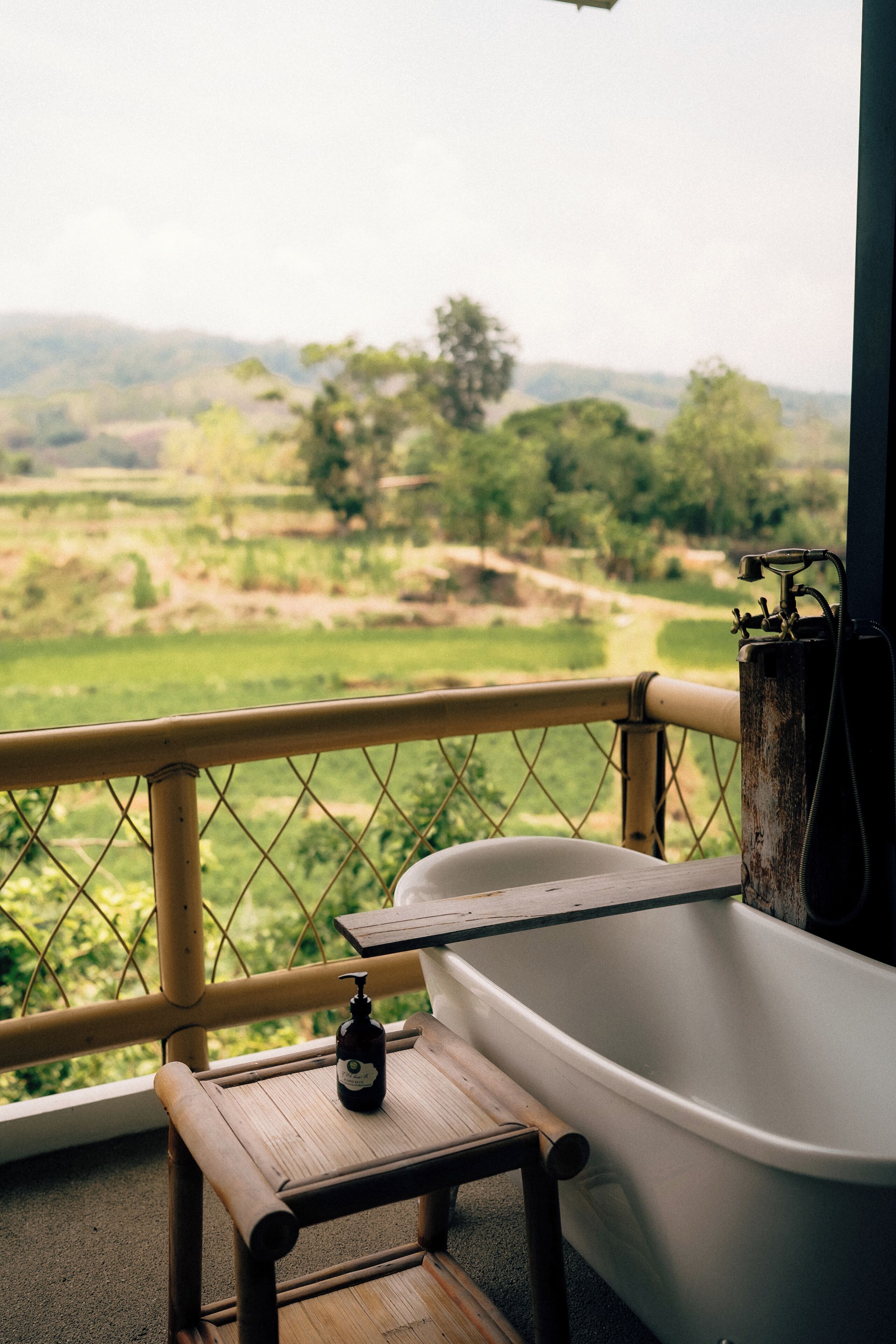 A bathtub on a balcony with a view of a green landscape.