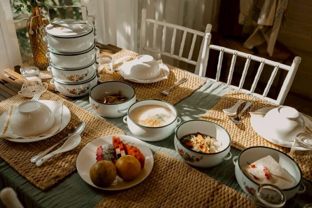 Ruokapöytä on katettu erilaisilla astioilla ja kulhoilla, ja sen ympärillä on valkoisia tuoleja.
