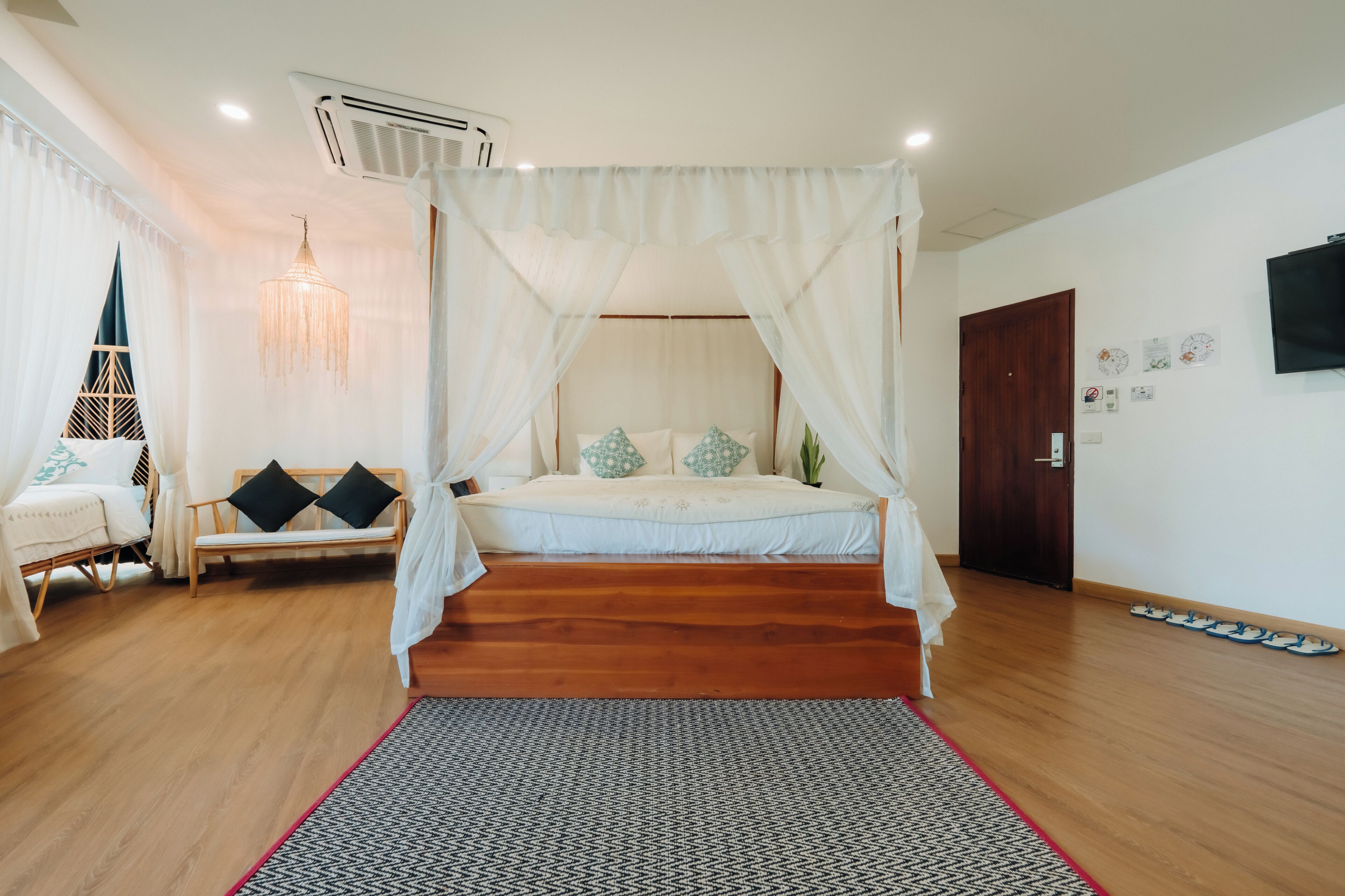 A bedroom with a canopy bed, a bedside table, a chair, a hanging light fixture, and a door.