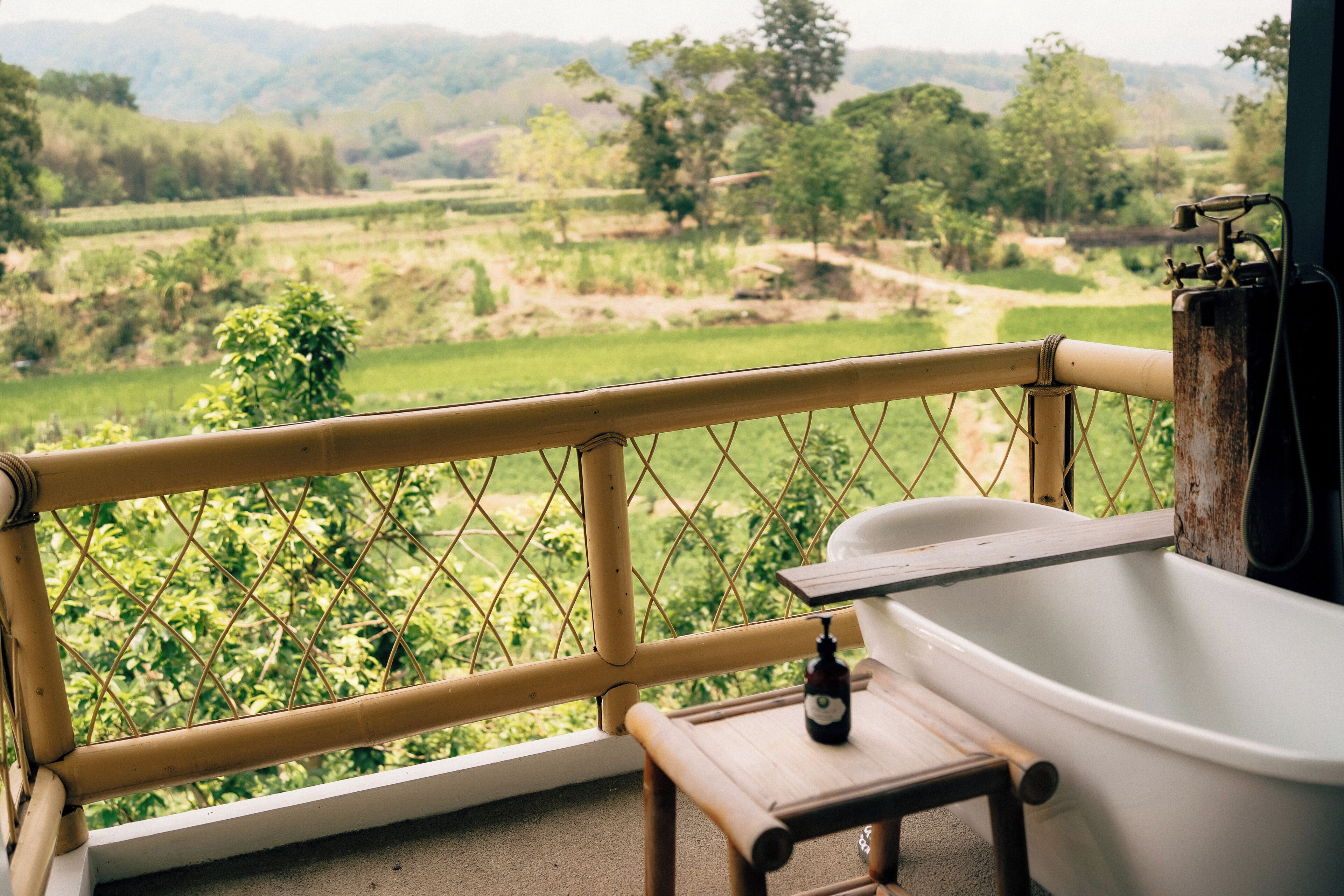 A balcony with a view of a green landscape, a bathtub, and a small wooden stool.