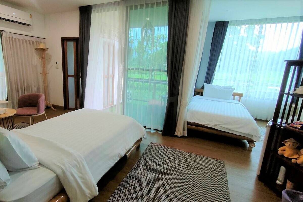 A hotel room with two beds, a sitting area with a chair and table, and a view of the outdoors.