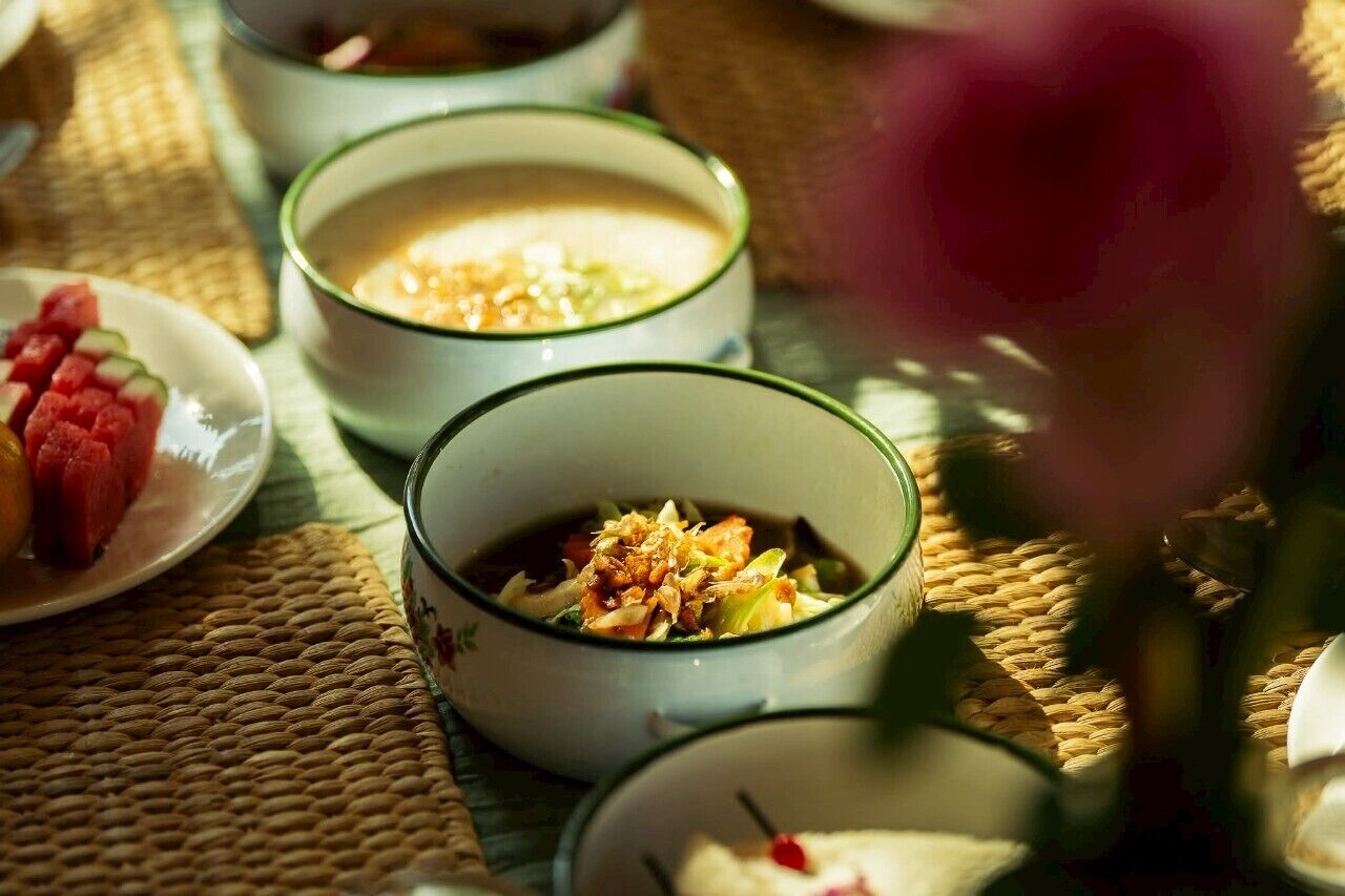Three bowls of soup on a woven mat, with a plate of sliced watermelon in the foreground.