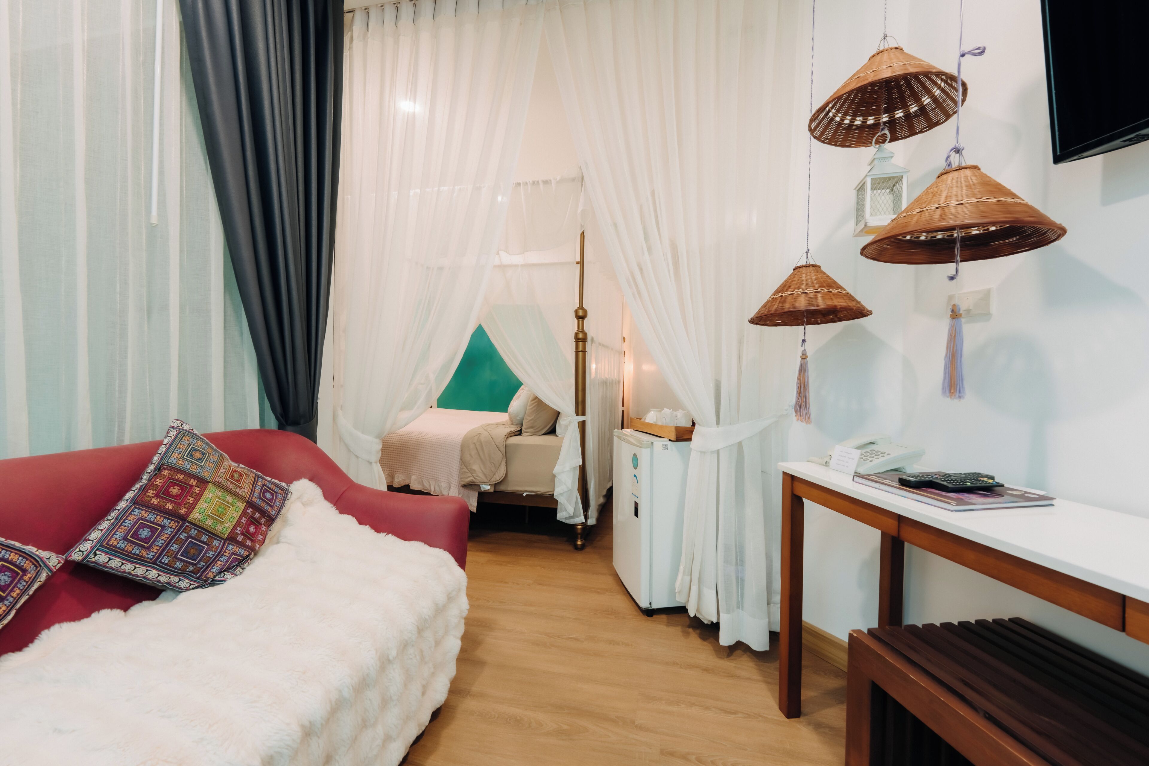 A room with a bed, a red couch, a wooden table, and a TV mounted on the wall.