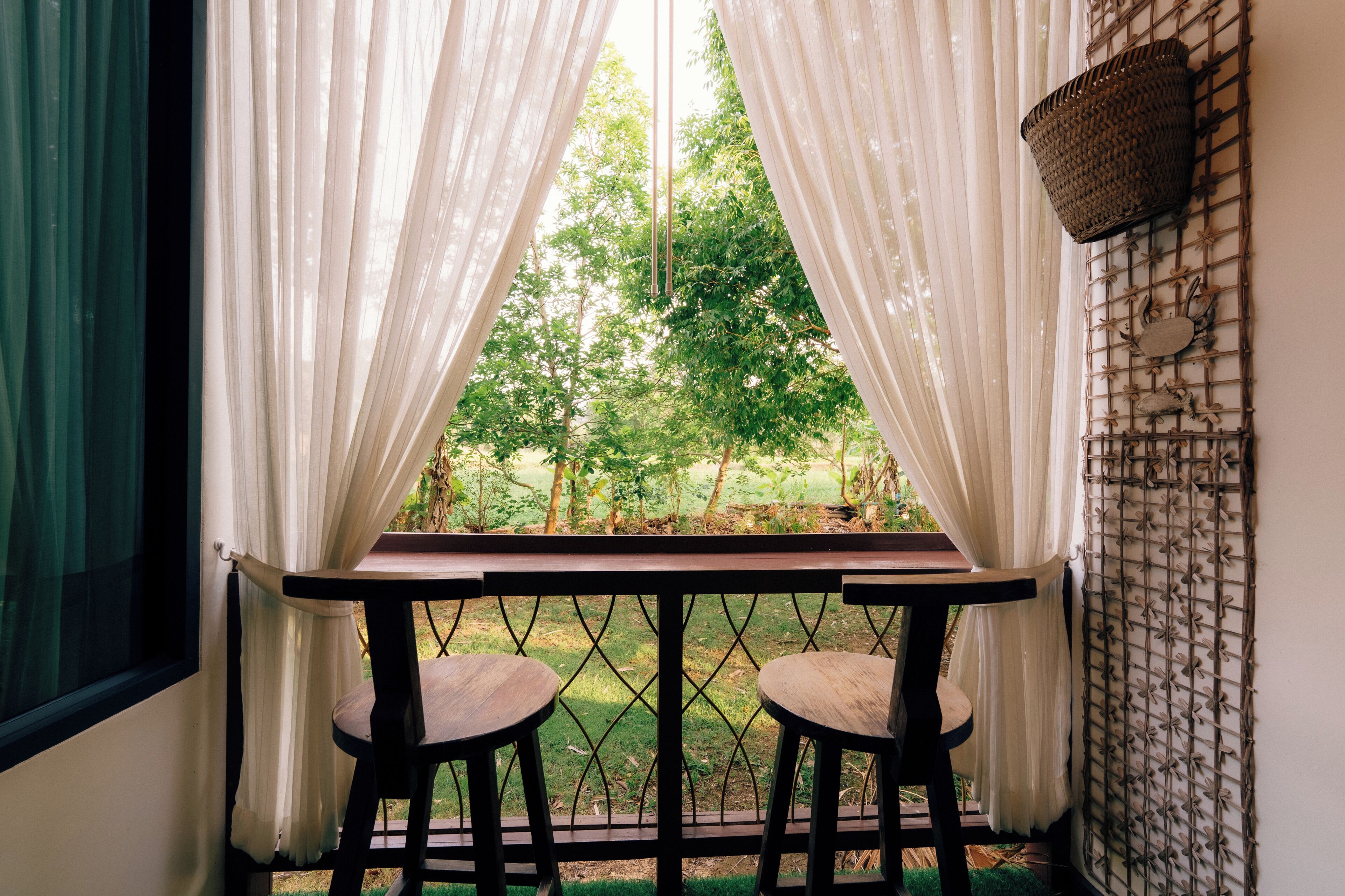 A window with white curtains, a table, and two stools.