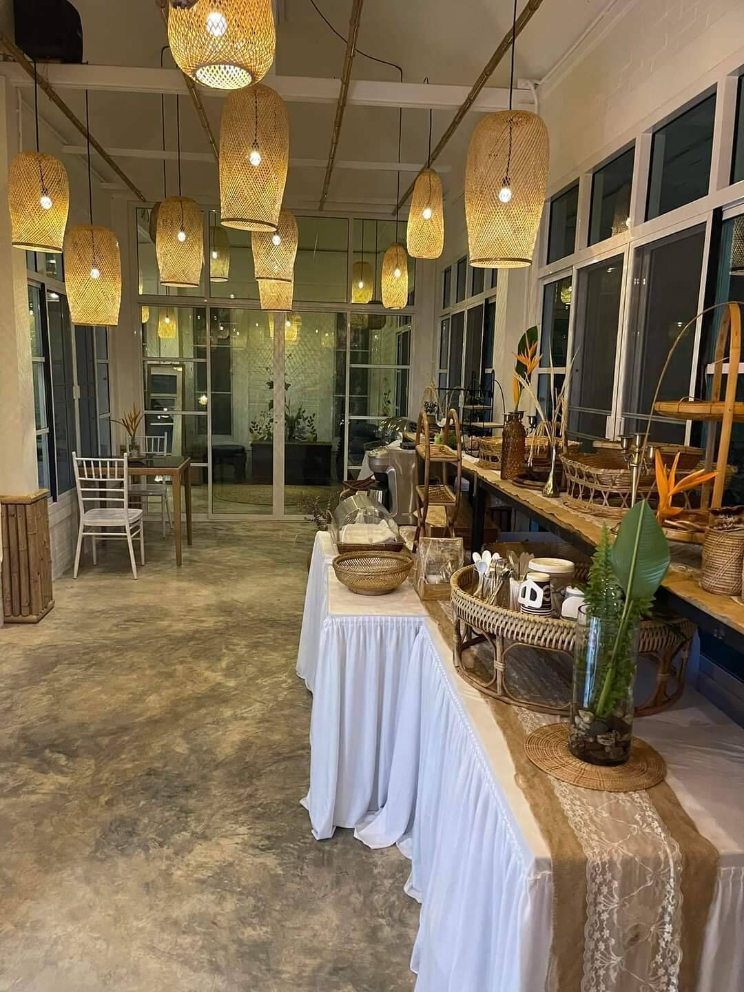 Un comedor con una mesa larga dispuesta para una comida, rodeado de muebles de mimbre y objetos decorativos.