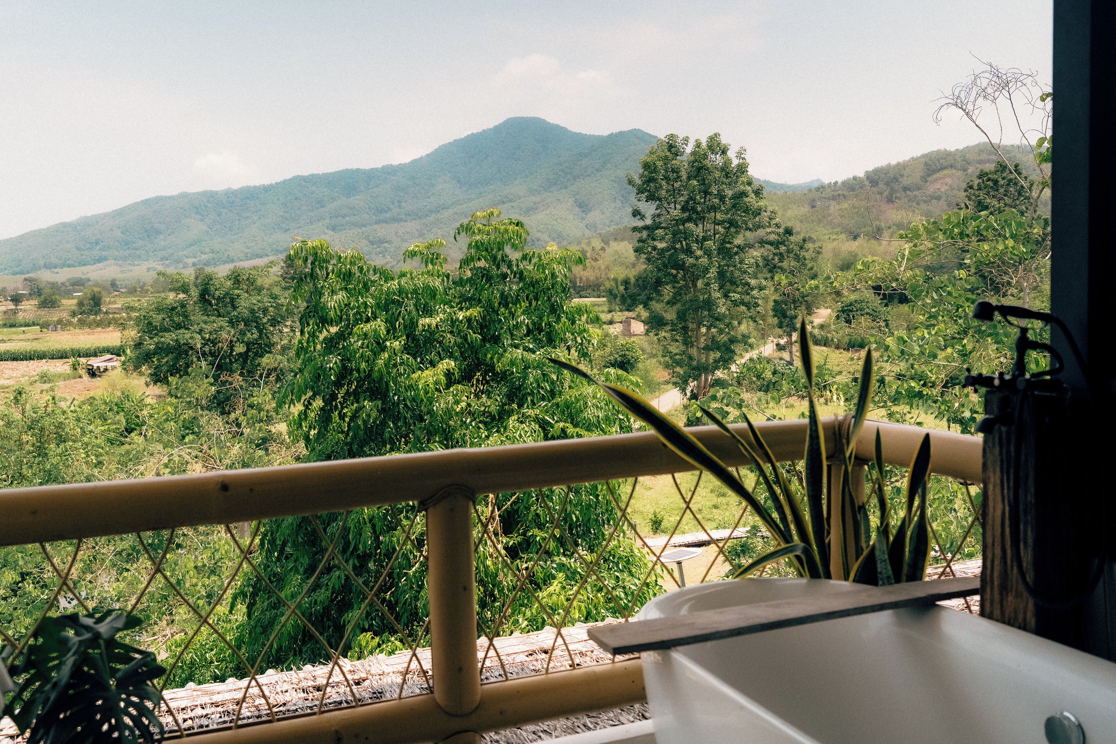 A balcony with a view of a mountainous landscape, a railing, and some greenery.