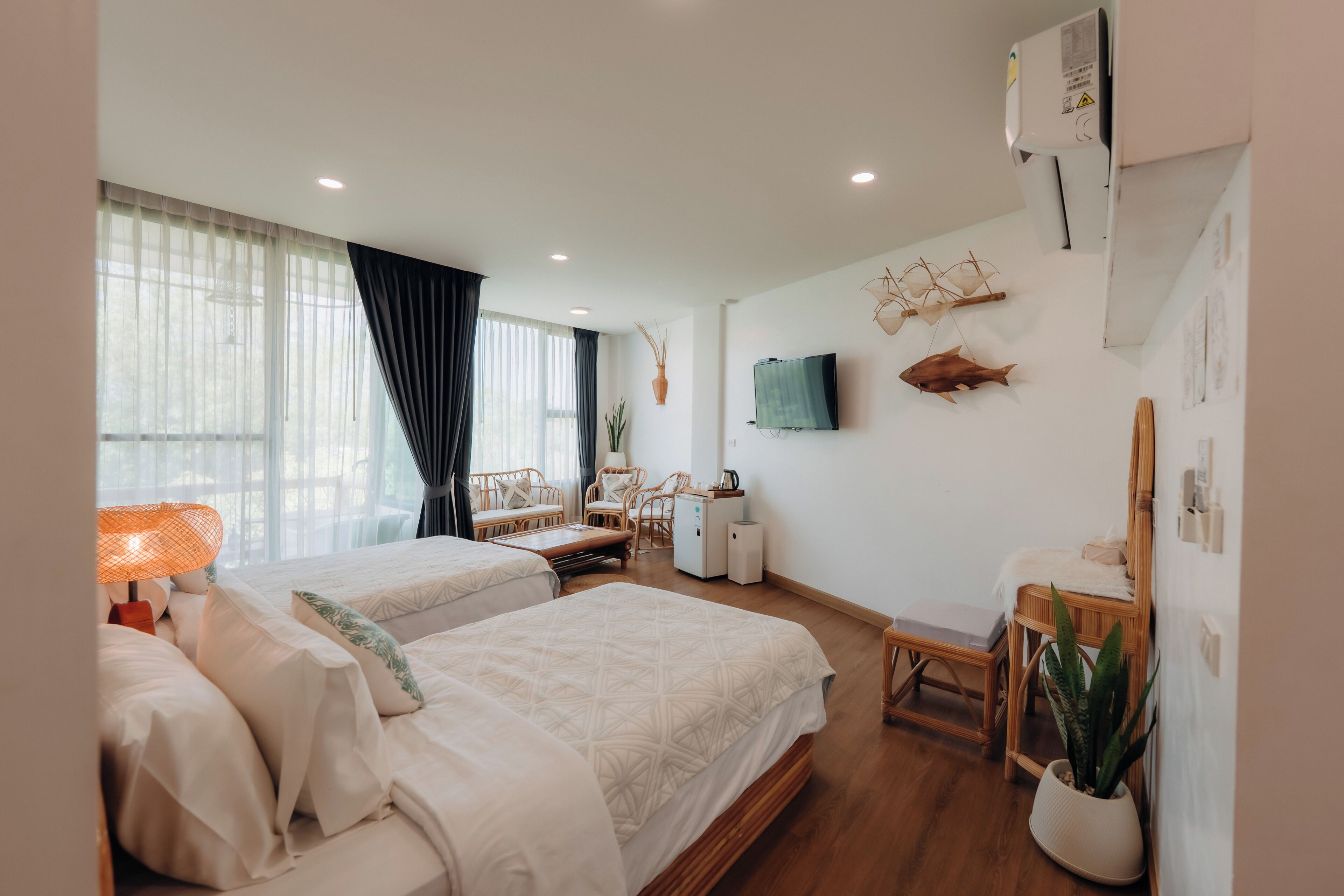 A hotel room with two beds, a desk, a chair, a TV, and a potted plant.