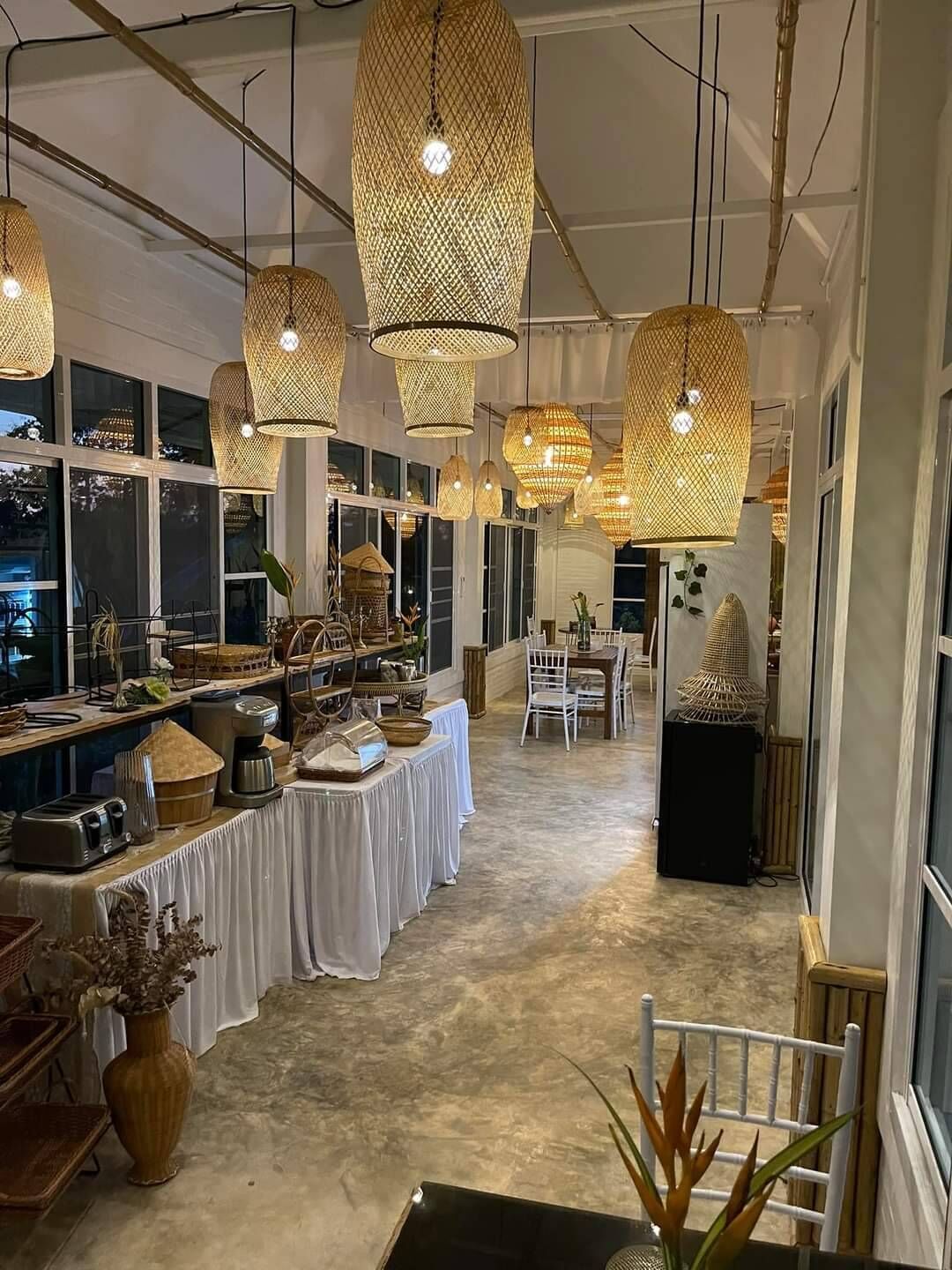 Un espacio amplio con ventanas grandes, una mesa larga con diversos objetos y múltiples lámparas colgantes de ratán.