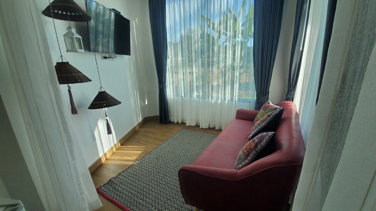 Una sala de estar con un sofá rojo, cojines estampados, un tapete tejido y lámparas colgantes.