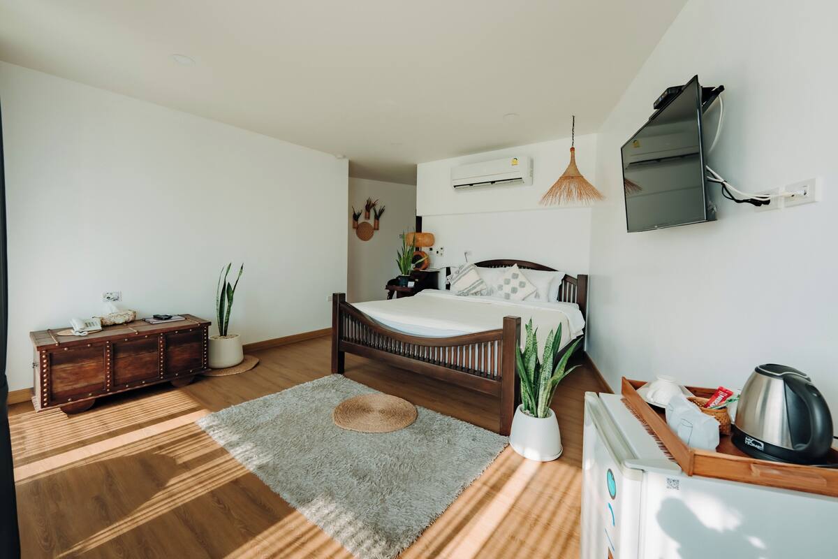 A bedroom with a wooden bed, a bedside table, a potted plant, a radiator, and a wall-mounted air conditioner.