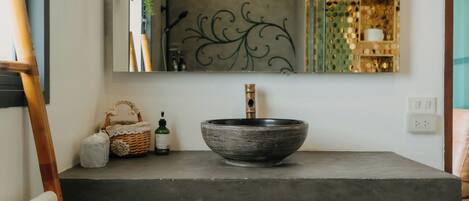A bathroom with a large mirror, a vessel sink, wooden cabinets, and a decorative wall piece.