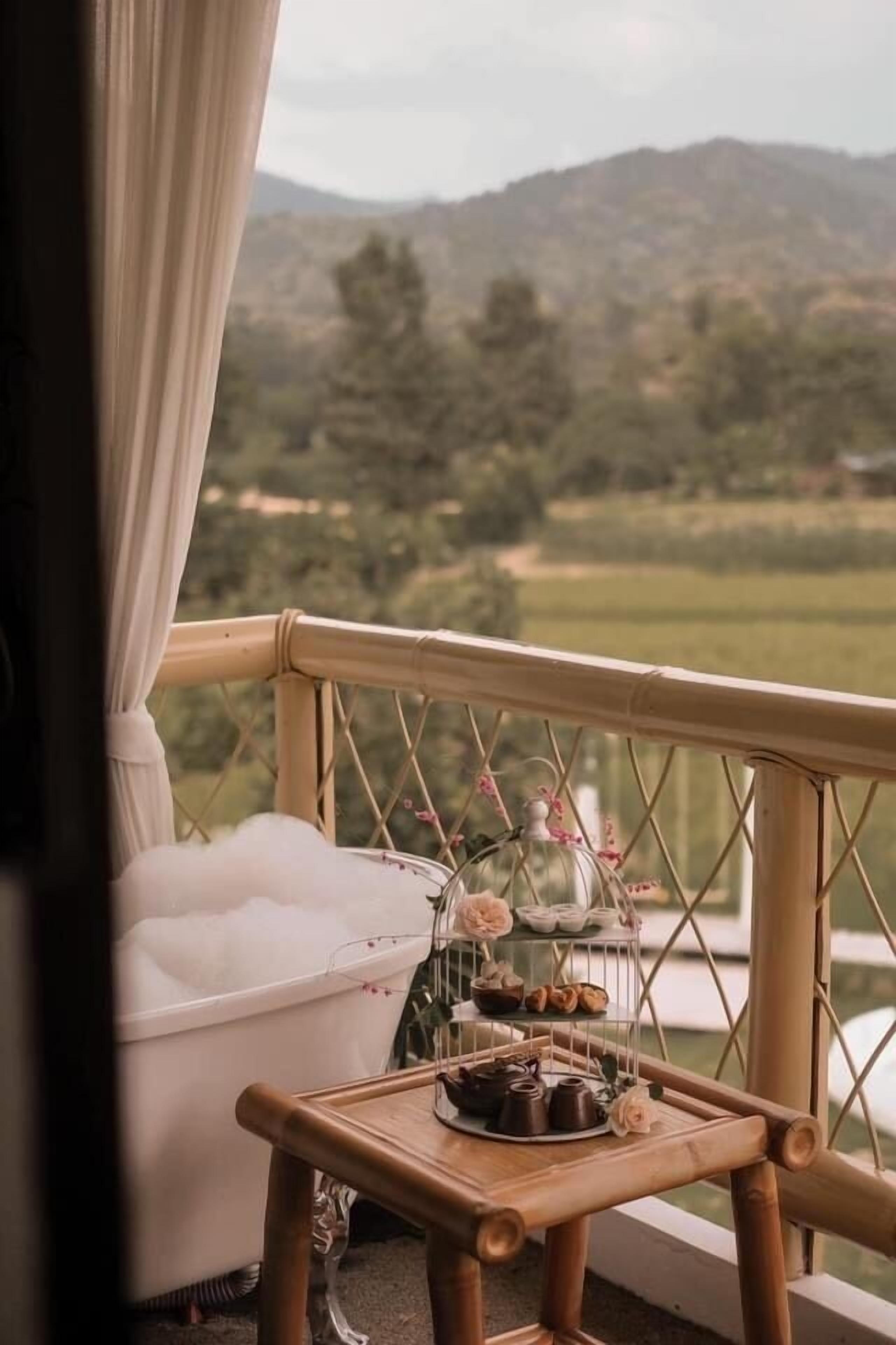 En balkon med et hvidt badekar, et træbord med bagværk og et glasmontre med blomster.