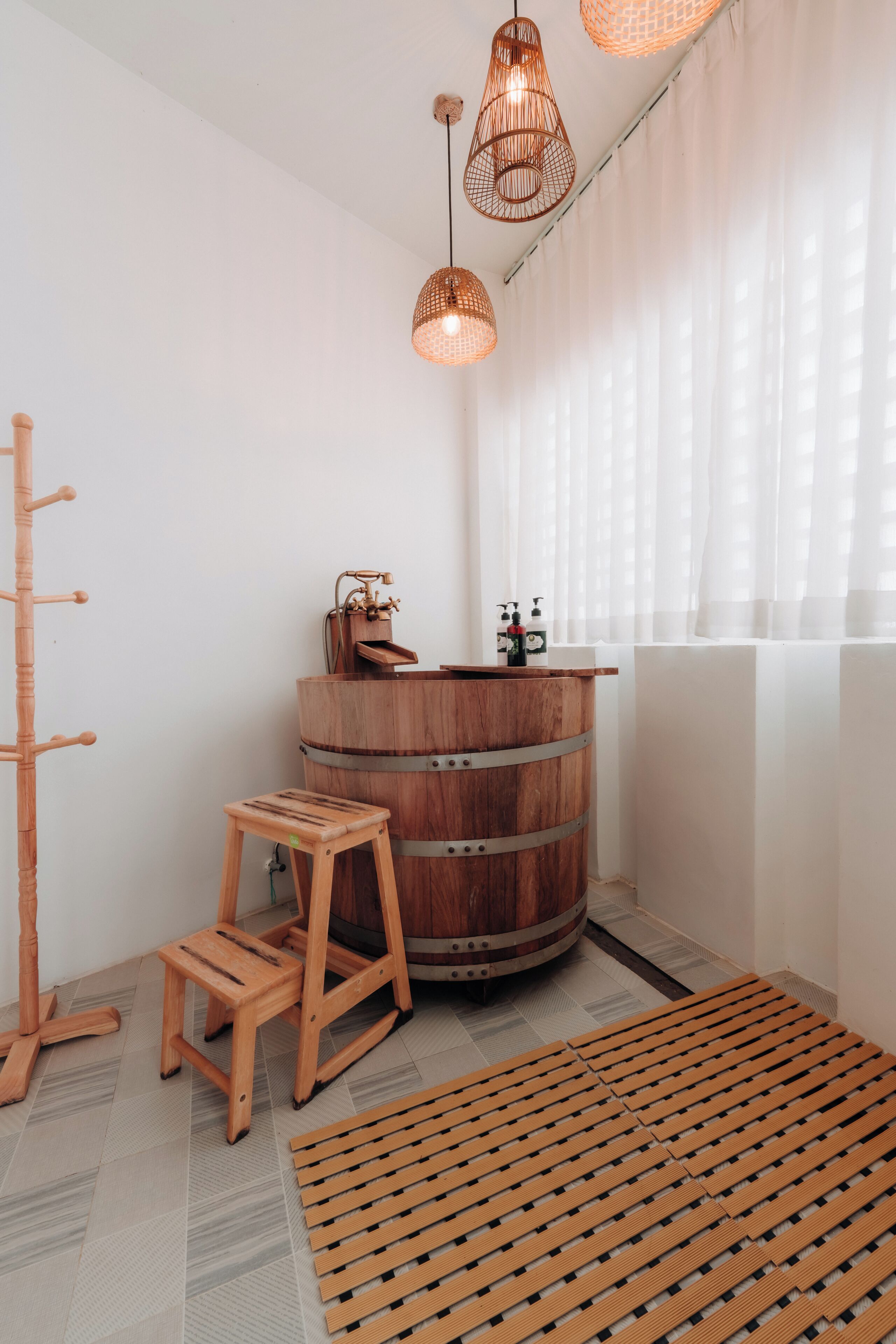 Une salle de bain avec un lavabo en forme de tonneau en bois, un tabouret en bois, une étagère en bois et un luminaire tressé.